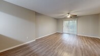 This single-story space is designed with a clean, neutral aesthetic that creates a cohesive and functional environment throughout. The living area is a standout feature, finished with light wood-look luxury vinyl flooring, neutral gray walls, and a ceiling fan overhead. A sliding glass door with vertical blinds allows natural light to filter in while offering views of lush outdoor greenery, enhancing the sense of openness and connectivity to the outdoors. An adjacent area with darker wood-look flooring provides a seamless transition toward the entryway, where a pass-through opening connects to the kitchen.

The kitchen is well-appointed with crisp white shaker-style cabinetry, light quartz countertops, and a full suite of stainless steel appliances, including a refrigerator, electric range, and built-in microwave. Light wood-look flooring completes the bright, modern feel of this space.

The bathroom is thoughtfully finished with a white vanity featuring ample cabinet storage, a large mirror with overhead lighting, wood-look flooring, and clean white fixtures. The bedroom offers plush dark carpeting, neutral walls, and a textured ceiling, providing a comfortable and quiet retreat. Overall, the space balances practicality with modern design details throughout.