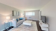 This single-floor residence presents a clean, contemporary aesthetic with a cohesive neutral color palette across all rooms. The spacious living room features rich dark hardwood flooring, a window-mounted air conditioning unit, and a baseboard heating system, offering comfort year-round. Natural light filters in through multiple windows, creating a bright and welcoming atmosphere.

The kitchen is well-equipped with white shaker-style cabinetry, granite countertops, a white tile backsplash, and a full suite of stainless steel appliances, including a refrigerator, electric range, and over-the-range microwave. Dark hardwood flooring continues seamlessly into the adjacent dining area, which features a sliding glass door providing additional natural light and outdoor access.

Two bedrooms are carpeted in warm neutral tones. The primary bedroom includes a built-in closet, an additional secondary door, a window with natural light, and a window-mounted air conditioning unit. The second bedroom is a comfortable, well-lit space with its own window and baseboard heating. The bathroom is finished with a full-size soaking tub and shower combination in crisp white, complemented by neutral tile flooring.