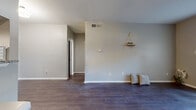 This single-floor residence is designed with a cohesive, modern aesthetic throughout. The open living area serves as the centerpiece of the layout, featuring dark hardwood-style flooring and light gray walls that create a clean, neutral backdrop. The ceiling in this space rises with a subtle vaulted angle, adding a sense of height and openness. A decorative rope-hung wall shelf provides a charming accent detail.

The galley-style kitchen is well-appointed, featuring gray cabinetry, granite-look countertops, and a full suite of stainless steel appliances including a dishwasher, refrigerator, and electric range. A pass-through window connects the kitchen to the living area, enhancing the open feel. The kitchen continues the dark hardwood-style flooring found throughout the unit.

The bedroom is a quiet, well-proportioned room with a large window that allows natural light and outdoor views, complemented by a ceiling fan for added comfort. The flooring continues seamlessly from the main living spaces.

The bathroom features gray cabinetry with brushed nickel hardware, a granite-topped vanity with an undermount sink, a large mirror, and a tub-shower combination. Dark wood-style flooring ties the bathroom's design to the rest of the home, creating a unified and polished overall aesthetic.
