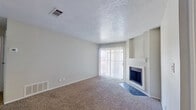 This single-story, 2-bedroom, 1-bathroom unit offers a functional and efficient layout across a compact footprint. The living room serves as the central gathering space, featuring carpet flooring, a textured ceiling, and a wood-burning fireplace with a tiled hearth and simple white mantel. A large sliding glass door with vertical blinds allows natural light to fill the room and provides outdoor access. The entry area connects directly to the living space, with wood-look flooring transitioning from the front door.

The galley-style kitchen runs along a narrow corridor and is well-equipped with gray cabinetry, granite-look countertops, a stainless steel sink, and black appliances including an electric range and refrigerator. Wood-look flooring extends throughout the kitchen, providing a clean, practical surface.

A carpeted hallway connects the bedrooms and bathroom. Both bedrooms feature neutral carpet, light gray walls, and windows with blinds that admit natural light. The primary bedroom offers a modest but functional space. The shared bathroom includes a gray vanity with a speckled countertop, a large mirror, wood-look flooring, and ample counter storage. The overall color palette is neutral throughout, creating a cohesive and understated ambiance.