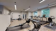 This modern fitness center is thoughtfully designed to support a comprehensive workout experience across a single open floor. The space features light wood flooring throughout, neutral gray-white walls, and a clean, contemporary aesthetic that promotes focus and energy.

The main workout area is generously proportioned, offering ample room to move between equipment zones. Multiple Concept2 rowing machines are positioned centrally on protective floor mats, accompanied by a row of treadmills and an elliptical trainer along the windowed wall. Large windows with horizontal blinds line the perimeter, flooding the space with natural light and providing pleasant views of the surrounding greenery.

A dedicated functional training section houses a cable and pulley machine, a stationary bike, and a balance dome, ideal for cross-training and rehabilitation exercises. A well-stocked accessory corner features a tiered rack of medicine balls, stability balls in multiple sizes, foam rollers, resistance bands, and a kettlebell rack with varying weights — catering to a broad range of fitness levels and training styles.

Linear pendant lighting runs across the ceiling, supplemented by recessed fixtures, ensuring the entire space is brightly and evenly lit. A mirrored wall in one section enhances the sense of depth and allows users to monitor form during exercise. Glass-panel doors connect to an adjacent room, adding to the facility's open and accessible feel.