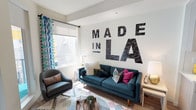 This single-floor residence captures the creative spirit of Los Angeles through thoughtful design and bold, artistic touches. The living room makes an immediate impression with a large "Made in LA" mural dominating the accent wall, serving as a striking focal point. The space is furnished with a mid-century modern teal sofa and coordinating armchair, layered with colorful throw pillows and a patterned area rug. A bright window dressed with geometric-print curtains and a roller shade allows natural light to fill the room, creating a warm and inviting ambiance. Hardwood-style flooring flows seamlessly throughout the unit, lending a cohesive, contemporary feel.

The kitchen is sleek and functional, featuring light wood-grain cabinetry, white quartz countertops, and a full suite of stainless steel appliances, including a range, microwave, dishwasher, and refrigerator. A white breakfast bar with seating offers a casual dining option.

The bedroom is a restful retreat, highlighted by a vibrant multi-colored polka dot wall mural above the bed. A large window with sheer curtains provides natural light, while a convenient walk-in closet adds practical storage.

The bathroom is clean and modern, with light wood-tone flooring, a white vanity, and a shower-tub combination, completing this well-designed urban residence.