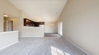 Located at 515 Timber Pointe Dr in Joliet, Illinois, this single-floor home is defined by its striking vaulted ceilings that rise dramatically throughout the main living area, creating a bright and airy atmosphere. The open-concept layout seamlessly connects the living room, dining area, and kitchen, making the space feel expansive and well-suited for both everyday living and entertaining.

The kitchen is equipped with dark espresso cabinetry, stainless steel appliances including a range, microwave, dishwasher, and refrigerator, and features light wood-look flooring that contrasts cleanly with the cabinetry. A raised breakfast bar separates the kitchen from the carpeted living and dining areas. An elegant chandelier provides overhead lighting, complementing the natural light that pours in through multiple large windows and a sliding glass door that opens to an outdoor area.

The bedrooms are carpeted and finished with neutral warm-toned walls, offering comfortable and quiet retreats. A walk-in closet with wire shelving provides generous storage. The bathroom includes a full tub-shower combination with clean white finishes and wood-look flooring. A dedicated utility room houses the water heater and laundry appliances. Throughout the home, clean white trim and a neutral color palette create a cohesive, move-in ready environment.
