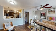 This single-floor residence offers a thoughtfully designed layout connecting the living, dining, and kitchen areas in an open, cohesive flow. The living room serves as the central gathering space, featuring rich dark hardwood-style flooring, a ceiling fan with integrated lighting, and a natural light source from a window with vertical blinds. A tufted camel-toned sofa anchors the room beneath a curated gallery wall, while a mirrored coffee table adds a reflective, modern touch.

The kitchen is well-equipped with dark cabinetry, light quartz countertops, a subway tile backsplash, and a full suite of stainless steel appliances, including a gas range, microwave, dishwasher, and refrigerator. Pendant lighting illuminates the peninsula counter, which opens toward the living area and provides additional workspace and casual dining potential.

Two bedrooms continue the dark hardwood-style flooring and feature ceiling fans, ample natural light from windows, and neutral wall tones. The bathrooms are outfitted with dark vanity cabinetry, quartz countertops, and updated lighting fixtures. One bathroom includes a long floating vanity counter with a large framed mirror, offering generous storage and prep space. The overall ambiance is modern and stylish with consistent design elements throughout.