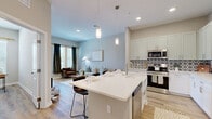 Located at 14355 North Main Street in Jacksonville, FL, this single-floor residence offers a thoughtfully designed layout with one bedroom, three bathrooms, and a flexible bonus room ideal as a home office or den. The open-concept kitchen and living area serves as the heart of the home, anchored by a large center island with a white quartz countertop, a farmhouse-style sink, and seating for casual dining. The kitchen is outfitted with white shaker cabinetry, stainless steel appliances, and a striking geometric patterned tile backsplash that adds a bold design accent. Elegant pendant lighting hangs above the island, illuminating the space with warm, inviting light. Light wood-look flooring flows throughout, complementing the soft, neutral color palette. The living area offers a bright and airy atmosphere with natural light filtering through large windows dressed in floor-to-ceiling drapes. The primary bedroom is generously sized with access to a well-appointed en-suite bathroom featuring a double vanity with granite countertops, framed mirrors, and a glass-enclosed walk-in shower. A spacious walk-in closet with built-in wire shelving provides ample storage. A dedicated laundry area and hallway complete the efficient floor plan.