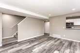 This two-story home showcases a cohesive modern aesthetic, with luxury vinyl plank flooring in warm grey tones flowing consistently throughout both levels. The main level features an open living area anchored by a staircase, recessed lighting, and a textured ceiling. A pass-through opening connects the living space to the kitchen, which is outfitted with crisp white shaker cabinets, striking marble-look quartz countertops, a stainless steel undermount sink, and a full suite of stainless steel appliances including a range, built-in microwave, and dishwasher. A window above the sink provides natural light and outdoor views.

The upper level hosts multiple bedrooms, each finished with the same vinyl plank flooring, neutral grey walls, and ample natural light from well-positioned windows offering green outdoor views. One bedroom features a ceiling fan and a closet. A full bathroom on this level includes a tub-shower combination with white surround panels and matching flooring. Additional rooms on the lower level benefit from recessed lighting, large windows, and direct exterior access through a paneled entry door, providing versatile living or flex space options throughout.