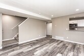 This two-story home showcases a cohesive modern aesthetic, with luxury vinyl plank flooring in warm grey tones flowing consistently throughout both levels. The main level features an open living area anchored by a staircase, recessed lighting, and a textured ceiling. A pass-through opening connects the living space to the kitchen, which is outfitted with crisp white shaker cabinets, striking marble-look quartz countertops, a stainless steel undermount sink, and a full suite of stainless steel appliances including a range, built-in microwave, and dishwasher. A window above the sink provides natural light and outdoor views.

The upper level hosts multiple bedrooms, each finished with the same vinyl plank flooring, neutral grey walls, and ample natural light from well-positioned windows offering green outdoor views. One bedroom features a ceiling fan and a closet. A full bathroom on this level includes a tub-shower combination with white surround panels and matching flooring. Additional rooms on the lower level benefit from recessed lighting, large windows, and direct exterior access through a paneled entry door, providing versatile living or flex space options throughout.