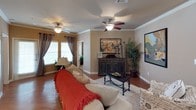 This single-floor residence offers a thoughtfully designed layout that balances comfort and functionality throughout. The living area is an inviting, open space finished with warm hardwood-style flooring, crown molding, and ceiling fans that lend a polished character to the room. Natural light filters in through multiple windows dressed with draping curtains, and an arched doorway adds an elegant architectural detail connecting the living space to the dining area and beyond.

The kitchen is well-equipped, featuring rich dark-wood cabinetry with modern hardware, light-toned countertops, a tile backsplash, and a full suite of stainless steel appliances including a range, microwave, dishwasher, and refrigerator. A double basin sink and generous counter space make this kitchen as practical as it is attractive. Light wood-style flooring continues underfoot.

The residence includes multiple bedrooms, each carpeted and fitted with ceiling fans. The bedrooms offer ample natural light through sizable windows and provide generous closet space, including walk-in closets with built-in shelving. One bedroom features a private en-suite bathroom with direct access to a well-appointed bath.

The bathrooms are finished with tile-surround tub and shower combinations, wood-style flooring, dark cabinetry for overhead storage, and neutral wall tones that create a calm, clean atmosphere throughout.