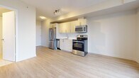 This efficiently designed 1-bedroom, 1-bathroom unit is laid out across a single floor, making smart use of every square foot. Light wood laminate flooring runs throughout the main living areas and bedroom, creating a cohesive and airy aesthetic. The open-concept kitchen and living area form the heart of the unit. The kitchen is outfitted with a full suite of stainless steel appliances — including a refrigerator, electric range, over-the-range microwave, and dishwasher — complemented by white cabinetry, a clean white countertop, and a subway tile backsplash. A large window in the living area allows generous natural light to fill the space while offering views of the surrounding greenery. The bedroom is a well-proportioned private retreat featuring warm wood flooring and a large built-in closet with sliding panel doors that maximize usable floor space. The bathroom is finished with white subway tile surrounding a soaker tub with overhead shower, a white vanity with an undermount sink, and light tile flooring, giving it a clean and functional character. A sliding door closet and an entry corridor with additional storage round out the unit's practical layout, making this a well-appointed space suited for efficient, modern living.