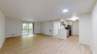 This 2-bedroom, 1-bathroom single-floor unit presents a clean, modern aesthetic defined by light wood-look flooring and crisp white walls that run consistently throughout the space. The open living area is generously sized, featuring a sliding glass door that leads to a private balcony overlooking mature trees, filling the room with natural light and greenery. A large window in the primary bedroom further enhances the connection to the outdoors, creating a bright and airy atmosphere.

The galley-style kitchen is efficiently designed with ample white cabinetry accented by gold hardware, white quartz countertops, and a full suite of stainless steel appliances including a refrigerator, dishwasher, range, and over-the-range microwave. The layout maximizes counter and storage space on both sides of the kitchen corridor.

The spacious primary bedroom offers generous square footage, providing comfortable room for furnishings and storage. The second bedroom is well-proportioned and similarly benefits from the consistent flooring and neutral palette. A dedicated closet adds practical storage to the unit.

The bathroom features a full tub-shower combination with white tile surround, a dark-toned vanity with gold hardware, and light wood flooring that ties in with the rest of the home. Textured ceilings are present throughout, adding a subtle design detail to the otherwise streamlined interior.