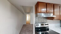 This single-floor, 2-bedroom, 1-bathroom residence offers a well-organized layout across a modest footprint. The galley-style kitchen is a functional highlight, featuring warm medium-toned wood cabinetry, marble-style countertops, a stainless steel refrigerator, dishwasher, and range, complemented by recessed lighting and light hardwood-style flooring. A decorative patterned tile backsplash adds a distinct visual element near the range area. The open connection between the kitchen and the carpeted main living area creates a natural flow through the unit.

Both bedrooms are carpeted and bathed in natural light through horizontal-blind-fitted windows that offer outdoor views of surrounding greenery. The primary bedroom includes a closet with a rod system, while the second bedroom also features its own closet, providing practical storage in each room. The hallway connects the bedrooms to the shared bathroom, which includes a white vanity with under-cabinet storage, a mirrored medicine cabinet, and light hardwood-style flooring. The neutral color palette throughout — white walls, beige carpet, and clean trim — contributes to a bright, cohesive ambiance across the entire unit.