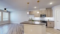 This well-appointed 1-bedroom, 1-bathroom unit offers a thoughtfully designed layout that maximizes every square foot. Light wood-tone flooring flows seamlessly throughout the entire space, creating a cohesive and airy feel.

The open-concept kitchen and living area serves as the heart of the unit. The kitchen is outfitted with flat-front cabinetry in a warm wood finish with brushed gold hardware, a white textured tile backsplash, stainless steel appliances, and a spacious island featuring a dark quartz countertop. Stylish globe pendant lights with gold fixtures hang above the island, adding a modern decorative touch. Built-in open shelving provides additional storage and display space.

The bedroom is a comfortable, well-proportioned retreat featuring a ceiling fan, natural light from dual windows with blinds, and neutral-toned walls that create a calm atmosphere.

The bathroom is notably well-equipped, featuring a double-sink vanity with dark countertops, wood-toned cabinetry with gold accents, a large mirror with contemporary lighting, and a frameless glass-enclosed walk-in shower adorned with full-height marble-style tile and matte black hardware.

A dedicated closet, hallway, and a private entry door with a glass panel complete this modern, move-in ready unit.