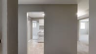 Located at 5685 Purdue Ave in Baltimore, MD, this single-floor 2-bedroom, 1-bathroom home offers a practical and well-organized layout. The kitchen is equipped with white cabinetry, dark stone-look countertops, a double sink, and full-size white appliances including a refrigerator and electric range, all set over neutral tile flooring. A connecting hallway links the main living areas efficiently, with a dedicated closet providing additional storage. The spacious primary bedroom features soft wall-to-wall carpeting, two windows that bring in natural light and outdoor greenery views, and a baseboard heating system. The second bedroom is similarly carpeted and bright, with its own window and baseboard heater, offering a comfortable and versatile space. Both bedrooms feature neutral gray-toned walls that complement the overall palette of the home. The full bathroom is clean and functional, featuring a soaking tub, toilet, pedestal sink, tile flooring, and a window for natural ventilation. Consistent neutral gray walls and white trim flow throughout the home, creating a cohesive and move-in-ready environment. The floor plan, as seen from the dollhouse view, reveals a sensible arrangement that maximizes the available living space.