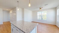 This well-appointed two-story residence offers a thoughtfully designed layout with modern finishes throughout. The heart of the home is the open-concept kitchen, which features crisp white cabinetry, a gray subway tile backsplash, and a generous granite-topped island with seating potential. A full suite of stainless steel appliances — including a refrigerator, range, microwave, and dishwasher — completes the kitchen. Stylish pendant lights illuminate the island, while the space flows seamlessly into the adjacent living and dining area, which benefits from abundant natural light through large windows and a ceiling fan overhead. Warm hardwood-style flooring runs throughout the main living areas, providing a cohesive and inviting aesthetic. A glass-paneled exterior door in the living area offers additional natural light and outdoor access. The bathroom is finished with a granite vanity countertop, white cabinetry, a large wall mirror, and a tiled shower-tub combination. Additional bedrooms feature the same warm hardwood-style flooring and clean white walls, offering versatile living spaces. A carpeted staircase with a warm wood handrail connects the two floors. The attached garage provides ample space for vehicles and features an automatic door opener for convenience.