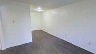 This single-floor space in Denton, Texas offers a clean, straightforward layout with a neutral design palette. The main living area is defined by dark hardwood-style flooring that contrasts with bright white walls, creating a simple yet functional aesthetic. The textured ceiling adds a subtle dimensional quality to the room, while a flush-mount ceiling light provides centralized illumination. White baseboards frame the perimeter of the room, adding a clean finish to the flooring transition. The walls are kept plain and free of architectural detailing, offering a blank canvas that can accommodate a variety of furniture arrangements and décor styles. The space feels open and uncluttered, with visible electrical outlets positioned along the walls for practical use. Overall, the interior presents a minimalist, move-in-ready environment suited for straightforward, functional living in the Denton area.