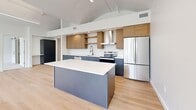 Located along the historic East South Temple corridor in Salt Lake City, this two-bedroom, two-bathroom residence offers a striking blend of architectural character and contemporary design. The living area is defined by soaring vaulted ceilings and a dramatic wall of floor-to-ceiling arched windows framed in sleek black steel, flooding the space with natural light and offering elevated views of the surrounding neighborhood, including a picturesque historic church. Light-toned hardwood flooring runs throughout the main living areas, enhancing the open, airy ambiance.

The modern kitchen is thoughtfully appointed with slate-blue lower cabinetry, warm wood open shelving and upper cabinets, white quartz countertops, a subway tile backsplash, stainless steel appliances, and a matte black faucet. A generous central island provides additional prep and gathering space beneath the dramatic vaulted ceiling.

Both bedrooms feature plush carpet, vaulted ceilings with clerestory windows, and generous closets equipped with built-in shelving and hanging rods. The primary bathroom offers a walk-in glass-enclosed shower, a warm wood vanity with white countertops, and a backlit mirror. The secondary bathroom includes a soaking tub-shower combo and a matching wood vanity, all finished with light hardwood flooring for a clean, cohesive look.
