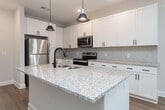 This single-story, one-bedroom, one-bathroom unit in Advance, NC is thoughtfully designed with a clean, contemporary aesthetic throughout. The open-concept layout connects the living room and kitchen, creating a cohesive and functional living space. Light wood-tone flooring runs through the main areas, reflecting natural light and contributing to a bright, airy atmosphere. Ceiling fans are present in both the living room and bedroom, adding comfort and practicality.

The kitchen is a standout feature, showcasing white shaker-style cabinetry with matte black hardware, granite countertops, a tile backsplash, and a central island with pendant lighting and an undermount sink. Stainless steel appliances, including a refrigerator, range, and over-the-range microwave, complete the space. The living area includes door access to the exterior, allowing natural light to pour in through slatted blinds.

The bedroom is carpeted for comfort and features a ceiling fan, windows with blinds, and access to a walk-in closet equipped with multi-tiered wire shelving. The bathroom mirrors the home's design language with a white vanity, granite countertop, and wood-tone flooring. Built-in open shelving adds convenient storage nearby.
