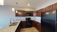 Located at 2803 Georgetown Rd in Lexington, Kentucky, this single-floor unit offers a thoughtfully designed layout with modern finishes and functional living spaces. The kitchen serves as a central highlight, featuring rich dark-wood cabinetry with brushed nickel hardware, speckled granite countertops, and a full suite of black appliances including an electric range, built-in microwave, and refrigerator. A peninsula with an undermount sink and pendant lighting above creates a natural divide between the kitchen and living area, making the space ideal for both everyday use and entertaining. Wood-look flooring runs throughout the main living areas, contributing a warm, cohesive aesthetic.

The bedroom offers plush carpeting, neutral gray walls, and natural light through a window with blinds. A closet with built-in shelving and hanging rod provides practical storage. The bathroom is designed with accessibility in mind, featuring stainless steel grab bars positioned at the toilet and along the shower area, with wood-look flooring continuing from the main living space. The overall color palette—soft grays, warm browns, and white trim—lends the unit a clean, contemporary feel throughout.