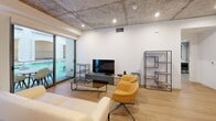 This contemporary 1150 square foot apartment, located in the TENTEN Downtown complex, offers a perfect blend of urban living and modern design. The space features two bedrooms, including a generous primary bedroom of 220 square feet, and two bathrooms, all spread across a single floor.

The apartment showcases an industrial-chic aesthetic with exposed concrete ceilings, creating a loft-like ambiance. Warm wooden floors throughout provide a pleasing contrast to the cooler tones of the concrete, resulting in a balanced and inviting atmosphere.

The kitchen is a highlight, boasting sleek cabinetry in a two-tone design of light wood and dark lower cabinets. Stainless steel appliances, including a large refrigerator with water dispenser, complete the modern culinary space.

Both bedrooms feature ample natural light from large windows, with the primary bedroom offering a spacious layout and built-in storage solutions. The bathrooms are elegantly appointed with modern fixtures, including glass-enclosed showers with rainfall showerheads.

The living area is open and airy, with a sliding glass door leading to a balcony. This outdoor space overlooks a unique water feature that runs along the building, adding a tranquil element to the urban setting.

The TENTEN Downtown complex itself is an architectural marvel, with its white facade punctuated by arched openings and wrought iron balconies, creating a harmonious blend of classic and contemporary design. The building offers residents a vibrant, downtown living experience with the comfort and style of a modern, thoughtfully designed apartment.