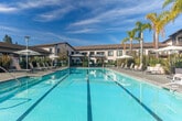 Located at 1101 N Fair Oaks Ave in Sunnyvale, California, this generously sized outdoor amenity space offers a resort-style experience within a residential community setting. The centerpiece is a large, clearly marked lap pool with pristine turquoise water, complemented by an ADA-compliant pool lift to ensure accessibility for all residents. The expansive pool deck surrounds the water on multiple sides, providing ample room for lounging and recreation under the California sun.

The deck is well-appointed with contemporary sling-style chaise lounge chairs and small side tables, arranged in clusters beneath large market umbrellas that offer shaded retreats throughout the day. Architectural pergola structures and covered pavilions frame one end of the pool area, creating comfortable semi-shaded gathering zones ideal for socializing or relaxing.

Thoughtfully designed landscaping enhances the ambiance, featuring tall palm trees, striking ornamental grasses, agave plants, and lush tropical foliage arranged in large raised planters. This curated greenery adds privacy, texture, and a vibrant, resort-like character to the space.

The surrounding multi-story building features modern architecture with large balconies, floor-to-ceiling windows, and clean contemporary lines, overlooking the pool area. Under abundant natural light and open blue skies, this outdoor space delivers a polished, inviting atmosphere well-suited for year-round enjoyment in the heart of Silicon Valley.
