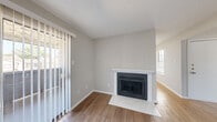 This single-floor residence offers a well-organized layout with a neutral color palette and consistent wood-style flooring running throughout the main living areas and bedrooms. The entry foyer provides an immediate view into the living space, with a wall-mounted thermostat conveniently positioned near the front door.

The living room serves as the focal point of the home, anchored by a classic fireplace with a white-trimmed mantel and a tiled hearth. A large sliding glass door fitted with vertical blinds admits generous natural light and provides outdoor access. An adjacent area offers additional flexible living or dining space, also benefiting from natural light through a side window.

The kitchen is efficiently designed with white cabinetry, white countertops, a stainless steel sink, subway tile backsplash, and a full-size stainless steel refrigerator. A secondary exterior door in the kitchen provides added convenience. The space also includes a washer and dryer area.

The bedrooms are comfortably sized, each featuring wood-style flooring, neutral walls, textured ceilings, and access to closet space. Windows fitted with blinds allow natural light while maintaining privacy. A full bathroom with a soaking tub completes the layout, as visible in the floor plan model.