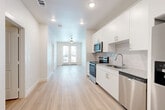 This thoughtfully designed one-bedroom, one-bathroom unit in Austin, TX offers a clean, modern aesthetic throughout. Light-toned luxury vinyl plank flooring flows seamlessly across the entire space, complementing the bright white walls and recessed lighting that keep the interior feeling open and airy.

The kitchen is well-appointed with a full suite of stainless steel appliances, including a range, microwave, dishwasher, and a side-by-side refrigerator with ice and water dispenser. White shaker-style cabinetry with brushed nickel hardware provides ample storage, while granite countertops and a classic subway tile backsplash add a polished finish. The kitchen opens directly into the living area, creating a practical and connected layout.

The living area is anchored by French doors that open to a private balcony, offering natural light and outdoor views. A ceiling fan keeps the space comfortable year-round.

The bedroom is a calm, well-lit retreat featuring a ceiling fan, a window with blinds for natural light and privacy, and access to a dedicated closet.

The bathroom features a full tub-shower combination with floor-to-ceiling warm-toned tile, a toilet, and built-in shelving for added storage. The overall design throughout the unit is clean, contemporary, and move-in ready.