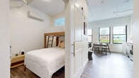 Located on the third floor at 174 E Long St in the heart of Columbus, Ohio, this thoughtfully designed one-bedroom, one-bathroom unit maximizes every square foot of its compact footprint. The open-plan kitchen and living area form the core of the space, featuring rich hardwood flooring throughout and large windows that flood the interior with natural light while offering views of the surrounding downtown Columbus cityscape. The kitchen is outfitted with stainless steel appliances, including a full-size refrigerator, electric range, microwave, and dishwasher, complemented by sleek gray cabinetry extending to the ceiling for ample storage. A dining area sits adjacent, making the space ideal for both cooking and entertaining. The living area provides a comfortable retreat with a wall-mounted mini-split HVAC unit for climate control. The bedroom is a cleverly engineered space featuring custom built-in bunk beds with a wood-ladder accent, maximizing sleeping capacity. A sliding barn door separates the bedroom from the main living area, adding a modern architectural touch. The bathroom is clean and contemporary, with a gray vanity, mirrored medicine cabinet, and a shower-tub combination. The bright, white walls and consistent hardwood flooring create a cohesive, modern aesthetic throughout.