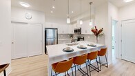 Located in the Nolan Hill neighbourhood of northwest Calgary, this single-floor unit offers four bedrooms and one full bathroom within a compact but efficiently arranged layout. Light hardwood-style flooring runs throughout the unit, complementing the crisp white walls that give the space a clean, modern aesthetic.

The kitchen is a standout feature, showcasing white shaker-style cabinetry, a grey tile backsplash, quartz countertops, and stainless steel appliances including a refrigerator, range, microwave, and dishwasher. Pendant lighting hangs above a generous island with bar seating for four, which connects seamlessly to the living area. The living room benefits from multiple windows fitted with roller blinds, allowing natural light while maintaining privacy. Baseboard heating is present throughout.

The four bedrooms vary in size, with the primary bedroom offering enough space for a queen bed and furnishings. Additional bedrooms are bright and versatile. The shared bathroom includes a single vanity with a white countertop, a large mirror, and a glass-enclosed stand-up shower. A walk-through area adjacent to the bathroom provides open shelving for storage. Outdoor views of the surrounding neighbourhood are visible from several windows.