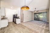 This efficiently designed single-story, one-bedroom, one-bathroom unit offers a thoughtful layout across a compact yet functional floor plan. The combined living and dining area serves as the heart of the space, featuring warm neutral-toned walls, plush carpeting, and a ceiling fan for year-round comfort. A sliding glass door in the living room opens to a private balcony, allowing natural light to flood the interior while offering pleasant outdoor views. The dining area is accented by a stylish dome pendant light and wood-look flooring, which also extends into the kitchen and bathroom.

The galley-style kitchen is well-equipped with white shaker cabinets, granite-look countertops, stainless steel hardware, a deep single-basin sink, and black appliances including an electric range with overhead microwave and a full-size refrigerator. The bathroom maintains a clean, modern aesthetic with white cabinetry, granite countertops, wood-look tile flooring, and a full tub-shower combination. The bedroom is a comfortable retreat with plush carpet, a ceiling fan with light, and a window fitted with blinds that provide natural light and privacy. Overall, the space presents a clean, neutral palette throughout.