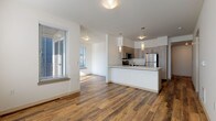 This single-floor unit offers a contemporary, open-concept layout that seamlessly connects the kitchen, dining, and living areas. Rich, warm-toned hardwood-style flooring runs throughout the main living spaces, creating a cohesive and inviting atmosphere. Large windows fitted with horizontal blinds allow abundant natural light to fill the space, and a sliding glass door in the living area provides access to an outdoor area.

The kitchen is well-appointed with light wood cabinetry extending to the ceiling for ample storage, stainless steel appliances including a refrigerator, range, and over-the-range microwave, and a white quartz peninsula countertop with an undermount sink. Pendant lighting above the peninsula adds a modern accent to the functional workspace.

The living area is generously sized with bright, white walls and multiple windows that maximize natural light. Two bedrooms feature plush neutral carpet, large windows, and clean, understated finishes that create comfortable, quiet retreats.

Both bathrooms are finished with light wood-toned vanity cabinetry, white quartz countertops, and full tub-shower combinations. One bathroom continues the hardwood-style flooring found throughout the unit, maintaining design consistency. The overall aesthetic is clean, modern, and move-in ready.
