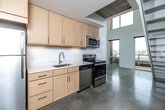 Located at 219 E Grand Ave in the heart of Des Moines, Iowa, this two-story loft offers a modern, industrial-inspired design across two well-proportioned floors. Polished concrete floors run throughout, lending a clean, contemporary aesthetic that ties the space together cohesively.

The main floor hosts the kitchen, which is outfitted with light maple cabinetry, white countertops, stainless steel appliances including a refrigerator, range, over-the-range microwave, and dishwasher, along with a single-basin sink. The open layout of the main floor is bathed in natural light from large windows and a skylight, with direct views of the surrounding Des Moines cityscape. A striking spiral staircase with an industrial metal frame connects the two levels.

The upper floor features an open loft area with exposed ductwork along the ceiling, recessed lighting, and a perforated metal railing that overlooks the main floor below. Large windows on this level provide continued urban views and abundant daylight.

The two bathrooms are finished in a clean, modern style, with one featuring mosaic tile surrounds, a soaking tub, and a wall-mounted sink. Additional conveniences include a dedicated closet with wire shelving and a hallway connecting the functional areas of the space. The overall ambiance is minimalist and urban, well-suited for a live-work lifestyle in downtown Des Moines.
