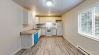 Located in Lakewood, WA, this 2-bedroom, 1-bathroom unit offers a well-organized, single-floor layout designed for comfortable everyday living. Light-toned luxury vinyl plank flooring flows consistently throughout, complementing the neutral beige walls and white trim that give the space a clean, cohesive aesthetic.

The kitchen is efficiently designed in an L-shaped configuration, featuring white cabinetry with ample storage, dark laminate countertops, and white appliances including a range, dishwasher, and refrigerator. It connects seamlessly to the combined living area, creating a practical open flow.

The living room is bright and welcoming, with a sliding glass door fitted with vertical blinds that opens to a private balcony overlooking greenery. A baseboard heating unit and an additional window allow for natural light and comfort throughout the seasons.

Both bedrooms are well-proportioned with textured ceilings, LVP flooring, and baseboard heaters. The primary bedroom includes a spacious reach-in closet with built-in shelving and hanging rods. Each bedroom features windows with blinds, bringing in natural light and outdoor views.

The full bathroom is clean and straightforward, equipped with a tub-shower combination, toilet, and vanity with a sink. A utility area in the hallway houses a water heater, adding practical functionality to the layout.