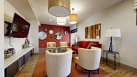Located at 3100 Park Ave in Tustin, CA, this well-appointed single-floor communal space offers a thoughtfully designed layout across a generous footprint. The interior is defined by a bold, contemporary aesthetic, with rich red accent walls, wood-look tile flooring, and curated artwork that create a warm yet energetic atmosphere throughout.

The primary lounge area features cream barrel chairs, a bold red sofa, and a striking gallery wall of round mirrors hung on a deep crimson accent wall. Pendant lighting in varying sizes illuminates the seating arrangement, adding visual depth and warmth. A second lounge area provides a more media-focused setting, with dual flat-screen televisions mounted on an orange accent wall, flexible ottoman seating on low-pile carpet, and natural light from nearby windows.

The open kitchen is a standout feature, equipped with dark cabinetry, tile backsplash, a gas cooktop, and a sleek white island with bar stool seating beneath amber pendant lights. Dual wall-mounted televisions add to the kitchen's functionality and appeal.

The dining area accommodates multiple seating configurations with modern tables and upholstered chairs, accented by tall indoor plants, abstract wall sculptures, and large windows offering views of an outdoor pool area. The space flows openly, making it well-suited for both social gatherings and everyday use.