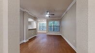 This 940-square-foot, single-floor apartment offers 2 bedrooms and 3 bathrooms in a thoughtfully designed layout. Warm hardwood-style flooring and elegant crown molding are consistent throughout the unit, creating a cohesive and polished aesthetic. The combined kitchen and living room serves as the heart of the home, with the kitchen featuring white shaker cabinetry, light stone countertops, a classic tile backsplash, and a full suite of stainless steel appliances including a range, over-the-range microwave, dishwasher, and refrigerator. The living room is bathed in natural light from multiple windows with outdoor views of surrounding greenery. Both bedrooms include ceiling fans with light fixtures, crown molding, and generous natural light. The primary bedroom measures 230 square feet and is complemented by a dedicated walk-in closet outfitted with wire shelving on multiple levels. The bathrooms are finished in neutral tones, with at least one featuring a full tiled tub-and-shower combination. A dedicated laundry room houses a full-size Whirlpool washer and dryer with overhead wire shelving for added storage. The unit is completed by an entrance foyer, offering a practical and welcoming transition into the living space.