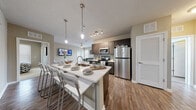 This single-floor residence in Tampa, Florida offers a well-designed, modern living environment with an open-concept layout that seamlessly connects the kitchen, dining, and living areas. The kitchen is a standout feature, showcasing dark espresso cabinetry, white quartz countertops, stainless steel appliances including a refrigerator, range, and microwave, a tile backsplash, and a large center island with bar seating and pendant lighting overhead — ideal for both cooking and entertaining. Wood-style flooring runs throughout the main living areas, adding warmth and continuity. The living room is bright and welcoming, with multiple windows dressed in white blinds that allow ample natural light, a ceiling fan, and direct access to an exterior door. Multiple bedrooms provide comfortable, private retreats, each featuring plush carpeting, large windows, ceiling fans, and sufficient space for a bed and desk setup. The bathrooms are clean and functional, finished with wood-style flooring, dark vanity cabinetry, white countertops, and tub-shower combinations with tile surrounds. The neutral, earthy color palette throughout the residence creates a cohesive, calm ambiance, making this Tampa home a practical and stylish space suited for everyday living.