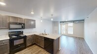 This one-bedroom, one-bathroom unit in Union, Box Elder, South Dakota offers a well-designed, efficient layout across a single floor. The open-concept kitchen and living area forms the heart of the space, where the kitchen stands out with dark espresso cabinetry, light granite-style countertops, a peninsula with an integrated double sink, pendant lighting, and black appliances including a range, microwave, dishwasher, and refrigerator. Wood-look plank flooring runs throughout the main living area, lending warmth and visual continuity.

The living room is bright and accessible, featuring a glass door that opens to a private balcony, allowing natural light to fill the space and providing outdoor views of the surrounding community. Exposed ductwork adds an industrial touch to the otherwise clean, neutral aesthetic.

The bedroom is carpeted for comfort and includes a window that brings in additional natural light. The full bathroom features a dark vanity with storage, a large mirror, and a tub-shower combination with tile-style flooring. A dedicated laundry room includes a full-size washer and dryer along with built-in wire shelving for additional storage.