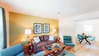 This two-floor residence is thoughtfully designed with a cohesive teal, olive, and warm wood color palette carried throughout each room. The living area serves as the heart of the home, featuring wood-style flooring, a textured ceiling, and a bold olive-green accent wall adorned with framed artwork. Comfortable seating surrounds a glass-top coffee table set atop a plush area rug, creating an inviting atmosphere. Adjacent to the living area, the dining space features warm hardwood flooring, a striking teal accent wall, and a pendant light fixture that illuminates a round dining table with seating for four. The kitchen is equipped with white cabinetry, dark countertops, black appliances including a range, microwave, and refrigerator, and a window above the sink that allows natural light to brighten the workspace. The bedroom offers carpet flooring, a teal accent wall, a window nook with bench seating, and a well-sized closet for ample storage. A second bedroom features neutral tones and an open closet. The bathroom showcases rich hardwood flooring, a vanity with extended countertop space, and a tub-shower combination. A dedicated laundry area with a full-size washer and dryer, complete with overhead shelving, adds everyday convenience to this well-rounded home.