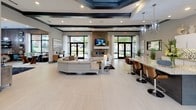 Located at 5270 Bryant Irvin Rd in Fort Worth, TX, this single-story community clubhouse showcases a sophisticated, contemporary design throughout. The welcoming entrance foyer features large floor-to-ceiling windows and glass doors that flood the space with natural light, complemented by elegant tray ceilings with a statement chandelier and light-toned large-format tile flooring that carries throughout.

The expansive main lounge serves as the heart of the facility, centered around a stacked-stone fireplace with a wall-mounted TV, framed by tall windows overlooking the surrounding greenery. A built-in granite bar with stylish barstool seating connects seamlessly to a full, well-appointed kitchen featuring white cabinetry, a mosaic tile backsplash, granite countertops, and a central island illuminated by modern chandelier pendants — ideal for resident gatherings and catered events.

A glass-walled business center provides a focused workspace with multiple workstations and views into the lounge. Adjacent to it, a lounge nook with a bold geometric-patterned accent wall, plush seating, a shuffleboard table, and dual wall-mounted TVs offers a relaxed entertainment retreat. A dedicated coffee and refreshment bar, also adorned with the striking patterned wall and mounted screens, rounds out the amenity offerings. The overall ambiance is polished, inviting, and thoughtfully designed for community engagement.