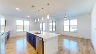 Located at 499 Commons Dr in Burleson, TX, this single-floor unit showcases a clean, contemporary design highlighted by a consistent palette of crisp white walls and light hardwood flooring throughout. The open-concept layout connects the kitchen and living area seamlessly, creating a bright, airy atmosphere enhanced by multiple windows that invite abundant natural light.

The kitchen is a standout feature, anchored by a large central island with a white quartz countertop, an undermount sink, and a stainless steel dishwasher beneath elegant pendant lighting. Bold navy shaker-style cabinetry with brushed nickel hardware lines the walls, complemented by a white subway tile backsplash and stainless steel appliances, including a range and microwave. The living area benefits from a ceiling fan and access to an outdoor space via glass doors.

A hallway connects the private areas of the unit, leading to well-proportioned bedrooms, each equipped with ceiling fans and windows offering natural light and exterior views. The bathroom features matching navy cabinetry with a white quartz vanity top, a framed mirror, and a glass-enclosed walk-in shower with neutral tile surround, maintaining the cohesive modern aesthetic found throughout the space.