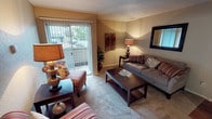 This single-floor residence offers a thoughtfully designed layout that balances comfort and functionality across its key living spaces. The living room serves as the heart of the home, featuring plush carpeting, warm neutral-toned walls, and a sliding glass door fitted with vertical blinds that opens to an outdoor patio, allowing natural light to fill the space. A framed wall mirror and coordinated accent lighting contribute to an inviting, cozy ambiance. The kitchen is efficiently arranged in a U-shaped configuration, showcasing warm wood cabinetry, granite-style countertops, and hardwood-style flooring. It comes fully equipped with a range, overhead microwave, dishwasher, and a full-size refrigerator, along with ample storage and a convenient pass-through counter that connects to the dining area. The bedroom is a serene retreat, appointed with soft carpeting, a window with curtains that allow for natural light, and generous space for furnishings including a full dresser and nightstands. Decorative wall art adds a personal touch to the room. The bathroom features a granite-topped vanity with a large illuminated mirror, a shower-tub combination, and tasteful finishes throughout. Overall, the space presents a warm, well-maintained interior with a practical and comfortable feel.