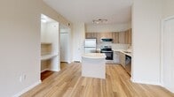Located on UTSA Blvd in San Antonio, TX, this single-story, one-bedroom, one-bathroom unit offers a thoughtfully designed layout with modern finishes throughout. The open-concept kitchen is a standout feature, equipped with stainless steel appliances including a refrigerator, range, microwave, and dishwasher, complemented by light wood-tone cabinetry, white countertops, and a kitchen island. Wood-look flooring runs through the main living and kitchen areas, adding warmth and continuity to the space. The bedroom is generously sized, featuring plush carpeting, a ceiling fan, and multiple windows that allow for natural light and views of the surrounding community. A hallway connects the living areas to the private spaces, which include a full bathroom outfitted with a wood-tone vanity, white countertop, a tiled shower-tub combo, and wood-look flooring. The walk-in closet offers ample storage with multiple wire shelving units running along the walls, providing well-organized space for clothing and accessories. A built-in nook near the living area adds a practical touch for display or workspace use. The overall aesthetic is clean and contemporary, with neutral tones creating a bright, cohesive ambiance throughout.