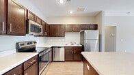 This single-floor residence is designed with a clean, contemporary aesthetic and an efficient open-concept layout. The kitchen serves as a central highlight, outfitted with rich dark-wood cabinetry, light-toned countertops, and a full suite of stainless steel appliances including a refrigerator, range, built-in microwave, and dishwasher. A generously sized center island provides additional counter space and creates a natural transition into the living area. Recessed lighting and light hardwood-style flooring contribute to a bright, cohesive atmosphere throughout.

The living area extends from the kitchen and is illuminated by natural light from a set of glass doors, complemented by a ceiling fan overhead. The neutral gray wall tones throughout the residence create a versatile backdrop suitable for a variety of décor styles.

The bedrooms are well-proportioned, each featuring ceiling fans, large windows with blinds, and access to closet space. One bedroom includes a walk-in closet with wire shelving and direct access to a private bathroom. Additional bedrooms feature standard reach-in closets. Light hardwood-style flooring runs consistently throughout all rooms, unifying the overall design of the space.