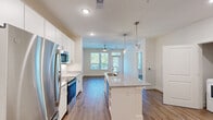 Located at 11201 Capital Blvd in Raleigh, NC, this thoughtfully designed one-bedroom, two-bathroom residence offers a contemporary living experience across a single, efficiently planned floor. The open-concept layout connects the kitchen and living areas seamlessly, creating a bright and welcoming atmosphere enhanced by natural light from multiple windows.

The kitchen is a standout feature, showcasing white shaker-style cabinetry extending to the ceiling, stainless steel appliances including a refrigerator, microwave, and range, a classic white subway tile backsplash, and a central island with a granite countertop and undermount sink. Pendant lighting above the island adds a modern touch, while durable wood-style flooring flows throughout the entire space.

The living area is airy and open, with a ceiling fan, large windows with views of surrounding greenery, and direct access to an entry door. The spacious primary bedroom features dual windows, a ceiling fan, and connects to a well-appointed bathroom with granite countertops and a walk-in closet with built-in shelving and drawers. A second bathroom provides added convenience for guests. Clean neutral walls, recessed lighting, and consistent flooring tie the entire space together cohesively.