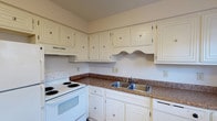 This two-story residence offers a practical and comfortable layout designed for everyday living. The kitchen features white cabinetry with decorative raised-panel detailing, dark granite-style countertops, a double stainless steel sink, a white electric range, and a dishwasher — providing ample storage and workspace for home cooking. Tile flooring completes the kitchen's clean, functional aesthetic.

Both bedrooms are generously proportioned, finished with plush wall-to-wall carpeting, and each equipped with a ceiling fan with light fixture for year-round comfort. Natural light filters in through blinds-covered windows, creating a bright and airy atmosphere. The rooms feature neutral wall tones and clean white baseboards throughout.

The full bathroom includes a tiled tub and shower combination with a curved curtain rod, offering a clean and classic look. A half bathroom provides added convenience and includes a closet with distinctive dark louvered bi-fold doors and tile flooring. A central staircase connects the two floors, featuring white balusters and wood-toned steps, anchoring the home's interior with a traditional architectural touch. Textured ceilings are present throughout the residence, adding subtle visual depth to each room.