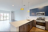This well-appointed 2-bedroom, 3-bathroom residence at 260 Avenue E in Bayonne, NJ offers a thoughtfully designed single-floor layout with modern finishes throughout. Wide-plank hardwood floors flow seamlessly across the living spaces, creating a warm and cohesive aesthetic.

The open-concept kitchen, dining, and living area serves as the heart of the home. The kitchen is a standout feature, showcasing bold navy cabinetry paired with wood-toned lower cabinets, a white quartz peninsula countertop, white subway tile backsplash, and a full suite of stainless steel appliances. Stylish pendant lighting adds a contemporary finishing touch.

The living area opens directly onto a private balcony through floor-to-ceiling sliding glass doors, filling the space with natural light and offering elevated views of the surrounding Bayonne neighborhood.

The primary bedroom is generously sized and includes a well-organized walk-in closet with built-in shelving and hanging rods. The secondary bedroom also benefits from large windows and ample natural light, along with dual closets for added storage.

All three bathrooms are finished with marble-look tile flooring and clean white subway tile. One bathroom features a soaking tub and shower combination, while another offers a glass-enclosed walk-in shower. A dedicated laundry area and utility room round out this practical and stylish residence.