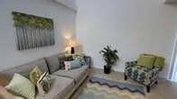 This two-floor residence offers a well-designed layout that balances comfort and functionality across its multiple levels. The living area immediately draws attention with its impressively high ceilings that lend an open, airy quality to the space. Neutral wall tones and light-colored carpet create a calm, versatile backdrop, allowing the furnishings and accents to stand out. The living room is thoughtfully arranged with a generous sectional sofa dressed in an array of colorful throw pillows, complemented by a patterned accent chair and a chevron-patterned area rug that adds visual interest underfoot. A floor lamp provides warm ambient lighting, while a decorative canvas artwork and a lush potted plant introduce natural elements that soften the interior. The clean lines and understated palette give the space a modern yet welcoming feel. The two-floor configuration allows for a natural separation between living and private areas, providing both open communal spaces and more intimate retreats. Overall, the residence combines practical design with thoughtful styling, resulting in a bright and inviting environment suited to everyday living.