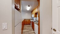 Located in Walnut Creek, CA, this 2-bedroom, 1-bathroom single-floor residence offers a well-organized layout across a comfortable footprint. The standout feature is the living room, which boasts a soaring vaulted ceiling clad in warm wood paneling, an expansive triangular clerestory window that floods the space with natural light, and a sliding glass door opening to a private balcony overlooking lush, mature trees. Light wood-plank flooring runs throughout the living areas, complemented by built-in glass shelving for display or storage. The galley-style kitchen is efficiently designed with warm honey-toned wood cabinetry, granite-effect countertops, a breakfast bar peninsula, white appliances, and hardwood-style flooring. A hallway connects the main living areas to the bedrooms, both of which feature plush carpeting and mirrored sliding-door closets. The generously sized primary bedroom offers ample space and natural light from a large window. The bathroom is well-appointed with a marble-effect tiled tub/shower surround with sliding glass doors, a wood-toned vanity with granite-style countertop, and light hardwood flooring. A textured ceiling is present throughout several rooms, adding a classic residential character to the home.