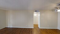 This single-floor unit offers a practical and comfortable layout with warm hardwood-style flooring running consistently throughout. The living area is bright and open, featuring a sliding glass door with vertical blinds that invites natural light and provides access to the exterior. A ceiling fan with integrated lighting fixture serves as a functional focal point overhead, while a dedicated HVAC vent ensures year-round climate control.

The kitchen is designed as a galley-style space, lined on both sides with warm-toned honey oak cabinetry offering ample storage both above and below the counters. White appliances, including a coil electric range, refrigerator, and dishwasher, are neatly integrated alongside a stainless steel sink. A pass-through counter connects the kitchen to the living area, enhancing the open feel of the space.

The bedroom features a notable textured concrete block accent wall that adds architectural character, complemented by a window with vertical blinds for natural light. Neutral, light-toned walls are present throughout, creating a clean and airy ambiance.

The bathroom includes a full-size soaking tub with a shower fixture and curved curtain rod, finished in a clean, neutral palette. The consistent flooring, thoughtful layout, and interconnected rooms make this a well-organized and easy-to-navigate single-level space.