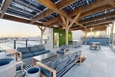 Located in Philadelphia's vibrant North Howard Street corridor, this rooftop terrace is a standout outdoor amenity defined by its striking solar-panel-integrated timber pergola. The heavy wooden beam framework spans the majority of the deck, housing an array of solar panels overhead while string lights add warmth during evening hours. Large-format porcelain tile flooring extends across the entire terrace, providing a clean, modern foundation throughout.

The lounge area beneath the pergola is furnished with generous sectional and accent seating in neutral tones, arranged around a coffee table atop a bold black-and-white striped area rug, with teak sun loungers positioned nearby for relaxed outdoor enjoyment. A lush vertical green wall serves as a dramatic living accent, framing the rooftop access entry and adding a vibrant natural contrast to the modern material palette.

The dining and bar area features a sleek standing-height island with bar stools alongside a separate dining table with woven rattan chairs, accommodating both casual and social gatherings. Unobstructed railing perimeters frame panoramic views of the Philadelphia skyline, offering a compelling urban backdrop at sunrise and sunset. This thoughtfully designed rooftop integrates sustainability, comfort, and style into a cohesive and functional outdoor retreat.
