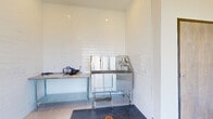 The Pointe Grand Pet Spaw is a purpose-built pet grooming facility designed to provide residents and their pets with a clean, functional, and well-equipped space. The single-level layout is finished with light-toned porcelain tile flooring and crisp white walls, creating a bright and hygienic environment throughout.

The main grooming area is the focal point of the space, featuring a professional-grade stainless steel bathing tub equipped with an attached spray nozzle system and a grooming arm. A stainless steel prep counter along one wall provides additional workspace, and a pet dryer is available for use. The walls in the grooming area are clad in glossy white subway tile, reinforcing the clean, utilitarian aesthetic while ensuring easy maintenance.

The entry area welcomes visitors through a glass door etched with the Pet Spaw logo and features a posted rules board outlining facility guidelines. Large floor-to-ceiling windows flood the interior with natural light and offer open views of the surrounding community grounds, including landscaped areas and residential buildings. A slim storage shelf and waste bin are thoughtfully placed near the window area for convenience. Safety features include a fire extinguisher station and an emergency exit sign, ensuring the space meets safety standards.